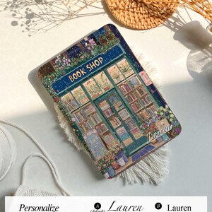 May include: A personalized phone case with a colorful illustration of a book shop with the text "BOOK SHOP" above the door. The case has a snowy background and the name "Lauren" is written in cursive on the bottom right corner.