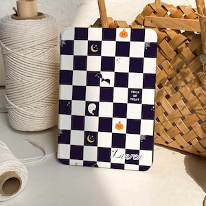 May include: A rectangular tablet case featuring a dark purple and white checkerboard pattern. The design includes small icons of orange pumpkins, yellow crescent moons, a black bat, a white ghost, and spiderwebs. The text reads TRICK OR TREAT and Lauren.