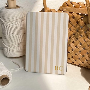 May include: A rectangular case with a cream and beige striped design. The initials "BC" are in gold on the lower right. A spool of white twine and a woven basket are in the background.