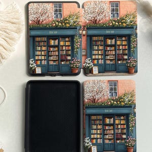 Op de afbeelding: Een zwarte Kindle Paperwhite hoes met een bloemenontwerp met een boekwinkel met de tekst "Book Shop". De hoes heeft een roze bakstenen buitenkant met een blauwe deur en een blauw raam. De hoes is open om een zwart interieur te onthullen.