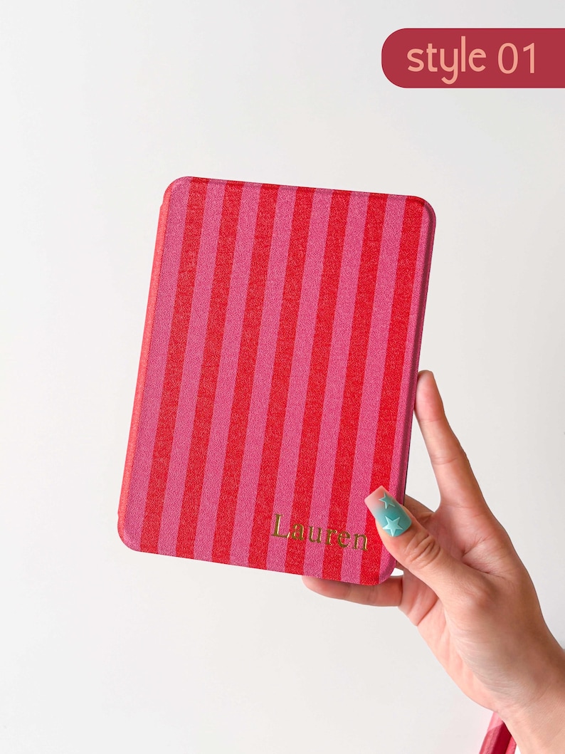 K&ouml;nnte beinhalten: Eine rechteckige E-Reader-H&uuml;lle mit vertikalem Streifenmuster in abwechselnden Rot- und Rosat&ouml;nen. Der Name Lauren ist in goldener Schrift nahe der unteren rechten Ecke aufgedruckt. Der Text style 01 erscheint in der oberen rechten Ecke.