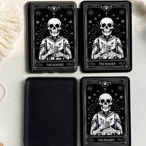 May include: Black and white tarot card design featuring a skeleton reading a book. The card is titled "The Reader" and is surrounded by stars. The card is on a black background.