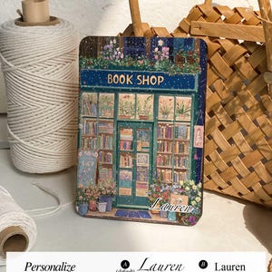 May include: A personalized phone case with a whimsical illustration of a book shop with a snowy backdrop. The text "BOOK SHOP" is above the shop, and the name "Lauren" is written below the shop.
