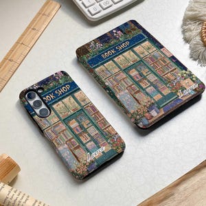 May include: Two phone cases with a book shop illustration. The cases are black with a green, blue, and white illustration of a book shop with the text "BOOK SHOP" above the door. The text "Lauren" is written in white on the bottom of each case.