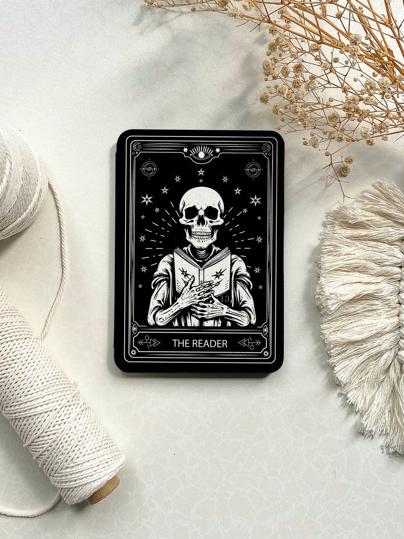 May include: Black and white tarot card with a skeleton holding a book. The card is titled "The Reader".