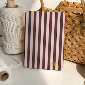 May include: A rectangular, pink and brown striped notebook with gold-colored initials "BC" in the bottom right corner. A roll of white twine and a woven basket are in the background.