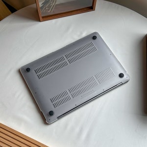 May include: The bottom of a silver laptop computer with black rubber feet. The laptop is on a white surface.
