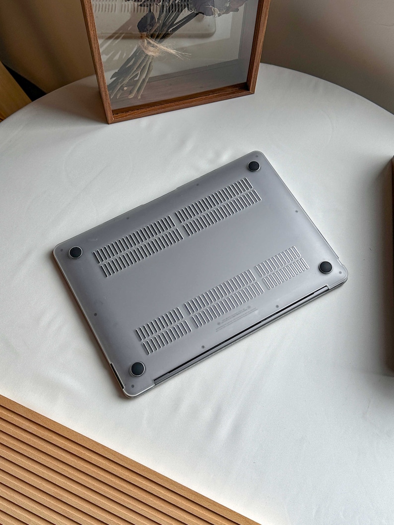May include: The bottom of a silver laptop computer with black rubber feet. The laptop is on a white surface.