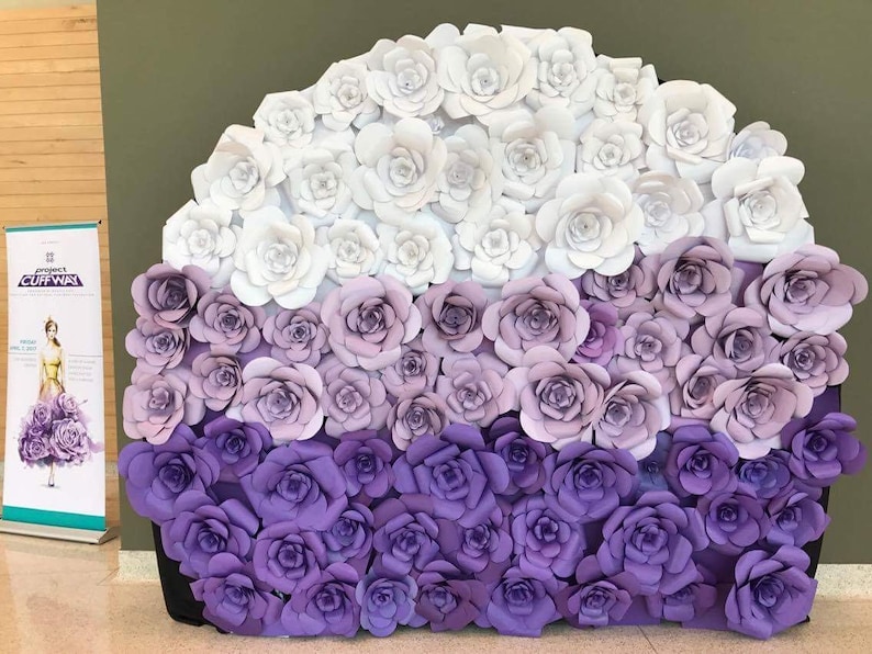 May include: A large, semi-circular display of paper roses in shades of white, lavender, and purple. The roses are arranged in a gradient, transitioning from white at the top to deep purple at the bottom. A banner on the left side reads "Project Cuffway".