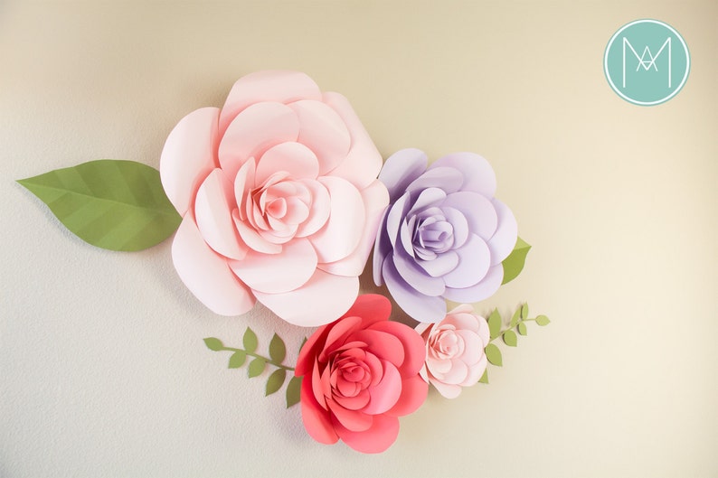 May include: A collection of large, handcrafted paper flowers in shades of pink, red, and purple, with green leaves and stems. The flowers are arranged on a light-colored background, creating a decorative floral display.