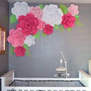 May include: A nursery with a white crib and a wall decorated with large paper flowers. The flowers are in shades of pink, white, and red, with green leaves. A mobile hangs above the crib.