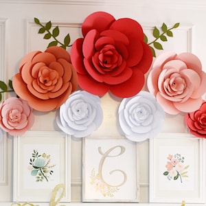 May include: A decorative arrangement featuring large paper flowers in shades of red, peach, pink, and white, accented with green leaf vines. Three framed floral prints are displayed below the flowers, creating a cohesive and artistic display.