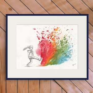 Op de afbeelding: Een ingelijste kunstdruk met een zwart-witte schets van een persoon die tegen een kleurrijke verfspat trapt. Het kunstwerk staat tegen een houten muur, met een zwarte luidspreker en groen in de voorgrond.