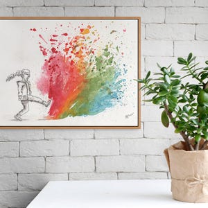 May include: A framed watercolor painting depicts a figure kicking a vibrant explosion of color. The artwork features a grayscale sketch of a person kicking into a burst of red, orange, yellow, green, and blue hues. A potted jade plant sits nearby.