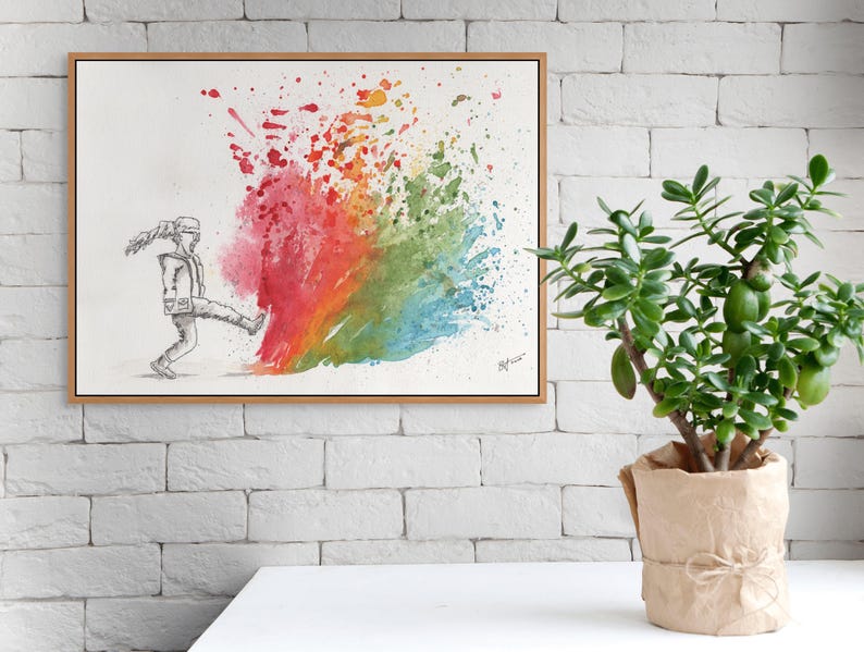May include: A framed watercolor painting depicts a figure kicking a vibrant explosion of color. The artwork features a grayscale sketch of a person kicking into a burst of red, orange, yellow, green, and blue hues. A potted jade plant sits nearby.
