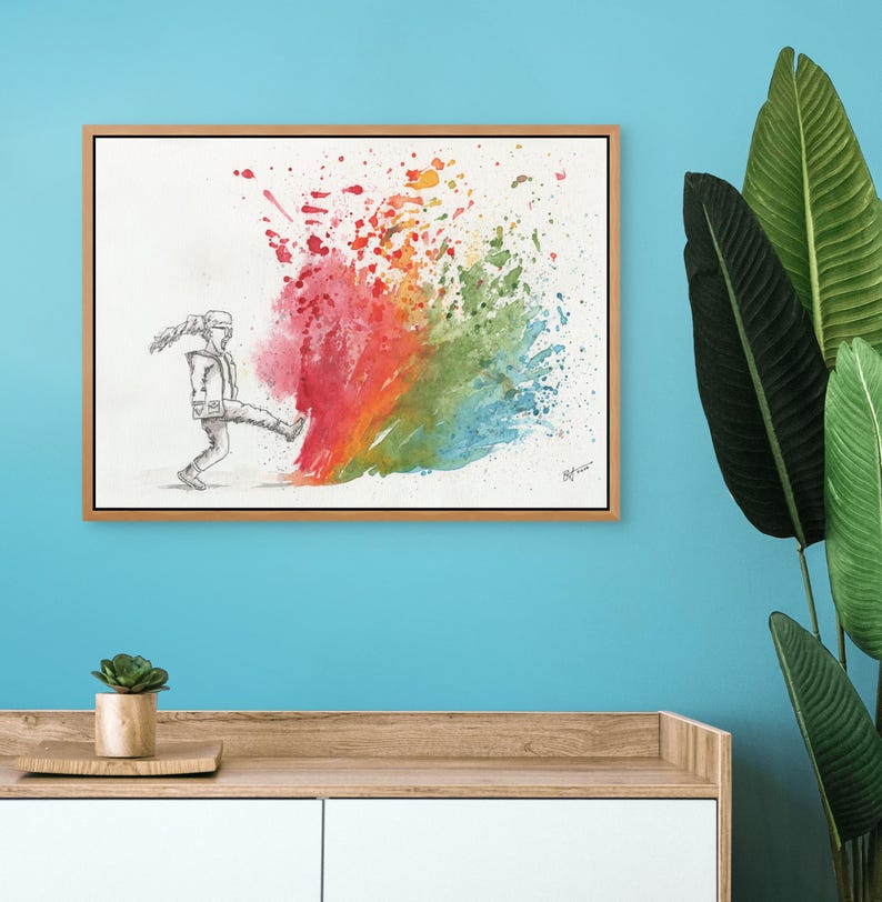 May include: A framed watercolor painting depicts a figure kicking a burst of colorful paint. The paint explosion features a vibrant spectrum of colors, including red, orange, yellow, green, and blue. The artwork is set against a white background.