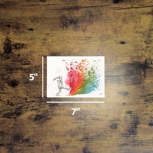 May include: A 5" x 7" watercolor painting on white paper. The artwork depicts a stick figure kicking a colorful splash of red, orange, yellow, green, and blue paint. The painting is on a wooden surface.