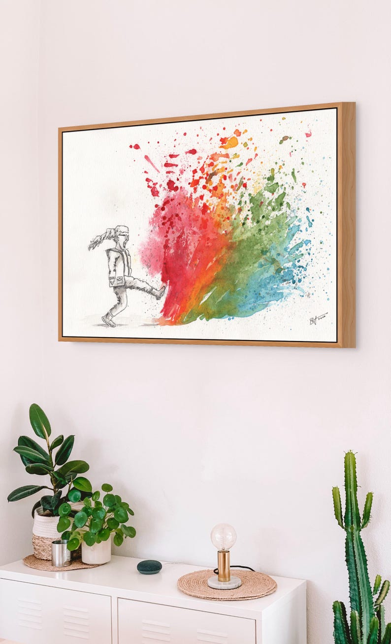 May include: A framed watercolor print depicts a figure kicking a vibrant explosion of color. The artwork features a person in grayscale kicking into a burst of red, orange, green, and blue hues. The artwork is in a wooden frame.