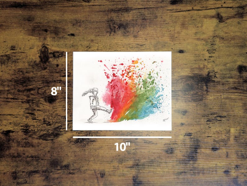 May include: An 8" x 10" watercolor print on a wooden surface. The artwork depicts a person kicking a colorful rainbow splash. The rainbow transitions from red to orange, yellow, green, and blue. The person is drawn in black and white.