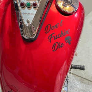 May include: A red motorcycle gas tank with the text "Don't Fuckin' Die" and a skull graphic. The tank also features a Kawasaki emblem and gauges.