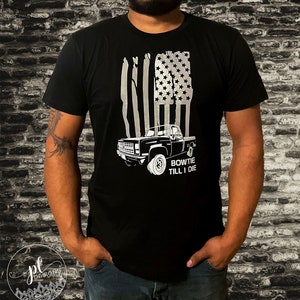 May include: Black t-shirt featuring a silver graphic of an American flag with a truck silhouette. The text "BOWTIE TILL I DIE" is below the truck. The shirt is short-sleeved.