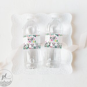 May include: Two clear plastic water bottles with labels that say "Going Wild & Three". The labels have a jungle animal theme with a zebra, rhino, and lion. The bottles are on a white plate with a white ribbon.