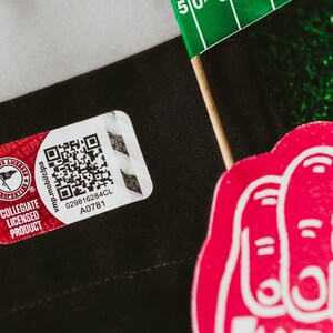May include: A red and white Collegiate Licensed Product tag with a black and white QR code. The tag has the text "vmp.mobilcpa 029816284CL A0781" printed on it.