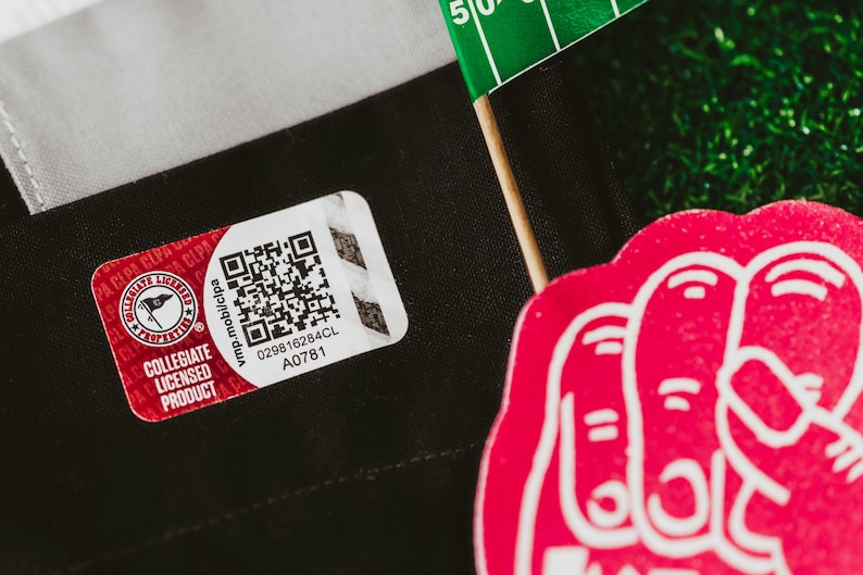 May include: A red and white Collegiate Licensed Product tag with a black and white QR code. The tag has the text "vmp.mobilcpa 029816284CL A0781" printed on it.