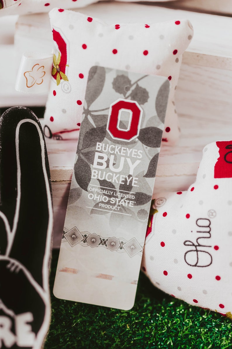 May include: A white and grey fabric tag with a red "O" and the text "Buckeyes Buy Buckeye. Officially Licensed Ohio State Product".