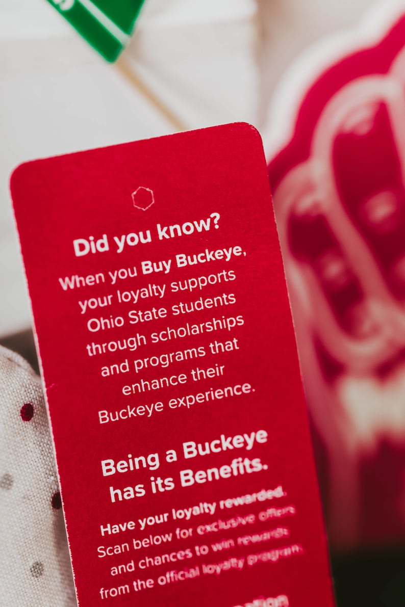 May include: A red card with white text that reads "Did you know? When you Buy Buckeye, your loyalty supports Ohio State students through scholarships and programmes that enhance their Buckeye experience. Being a Buckeye has its Benefits. Have your loyalty rewarded. Scan below for exclusive offers and chances to win rewards from the official loyalty programme."