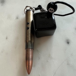 May include: A brown and copper bullet-shaped keychain with a black and silver 8-ball charm attached to a black cord.