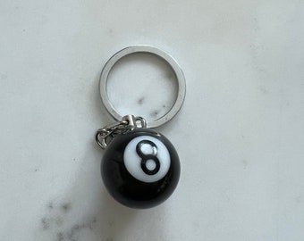 May include: A black and white 8 ball keychain with a silver key ring.
