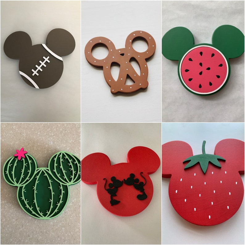 May include: Set of ten wooden ornaments featuring various Disney characters. The ornaments are painted in bright colors and feature details like Mickey Mouse ears, a red pretzel, a watermelon, a strawberry, and a cactus.