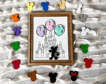Könnte beinhalten: Ein Set bunter Mickey Mouse Ohren mit einer Schwarzweißillustration von Mickey Mouse vor einem Schloss. Die Ohren sind aus Holz und haben eine Vielzahl von Farben, darunter Rot, Grün, Blau, Gelb und Lila.