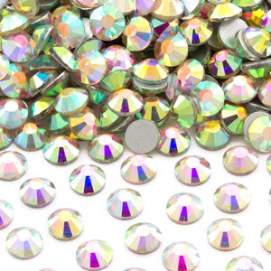 May include: A pile of iridescent clear rhinestones, with a few scattered on a white surface.