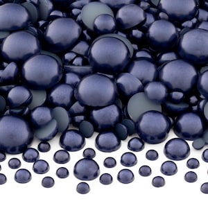 May include: A large pile of dark blue pearl-like round cabochons of various sizes. The cabochons are arranged in a random pattern and are scattered across the surface.