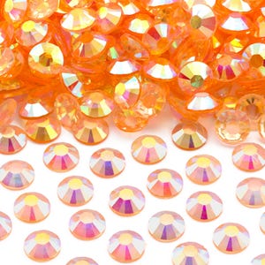 May include: A pile of orange iridescent rhinestones, with a row of smaller orange iridescent rhinestones spread out below.