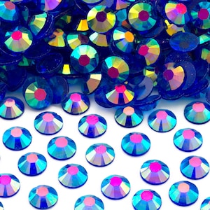 May include: A pile of iridescent blue rhinestones with a rainbow effect. The rhinestones are scattered on a white surface.
