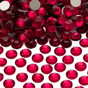 May include: A large pile of bright red rhinestones with a few silver adhesive backs visible. The rhinestones are scattered on a white background.