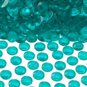 May include: A large pile of teal blue round plastic gems. The gems are scattered on a white surface.