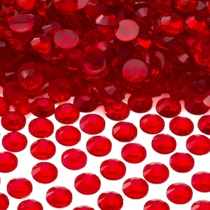 May include: A pile of red, round, faceted glass gems. The gems are scattered on a white surface.