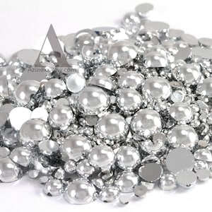May include: A large assortment of silver-colored round and flat embellishments. The embellishments are various sizes and have a shiny, reflective finish.