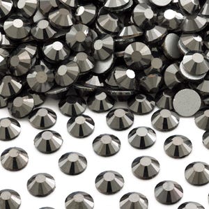 May include: A pile of black rhinestones, with a few scattered on a white surface.