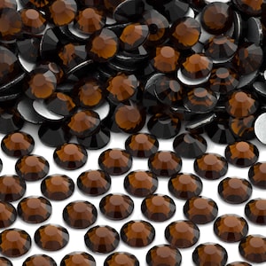 May include: A collection of faceted, brown rhinestones with a dark, almost black, base. The rhinestones are round with a flat back and a reflective surface. The image is a close-up, showing the details of the gems.