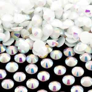 May include: A pile of iridescent white rhinestones, some with a flat back and some with a pointed back, on a black background.