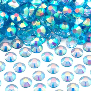 May include: A pile of iridescent blue rhinestones, with a scattering of smaller rhinestones in the foreground.