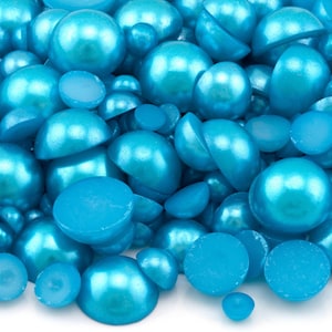 May include: A large pile of turquoise blue pearl cabochons. The cabochons are various sizes and shapes, some are flat and some are round.