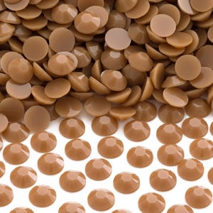 May include: A large pile of brown, round, flat-backed rhinestones. The rhinestones are arranged in a single layer on a white surface.