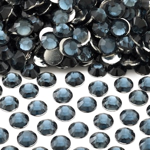 May include: A large pile of dark blue rhinestones with a smaller group of rhinestones spread out on a white background.