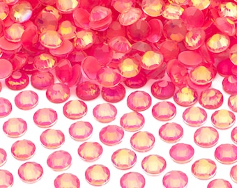 May include: A pile of iridescent pink round rhinestones, with a flat back, scattered on a white surface.